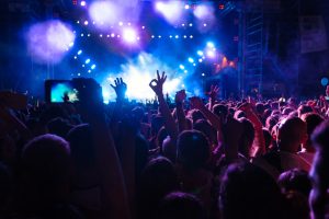 Crowd with raised hands at a concert, colorful lights shining from the stage