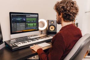 A person with curly hair sits at a desk using a computer for music production